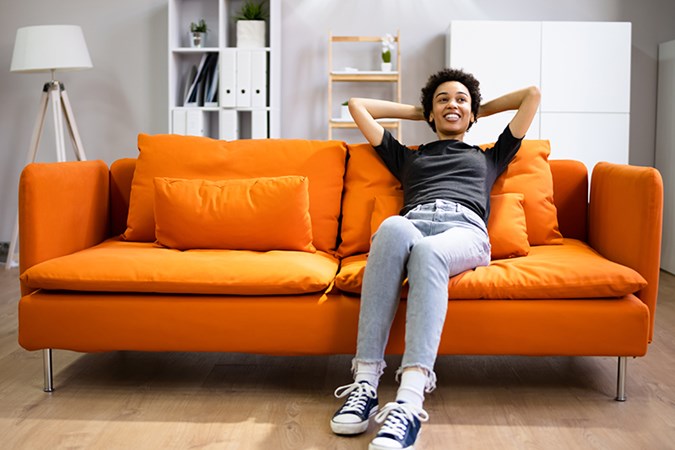 Kvinna som sitter bakåtlutad i en orange soffa i ett ljust rum.