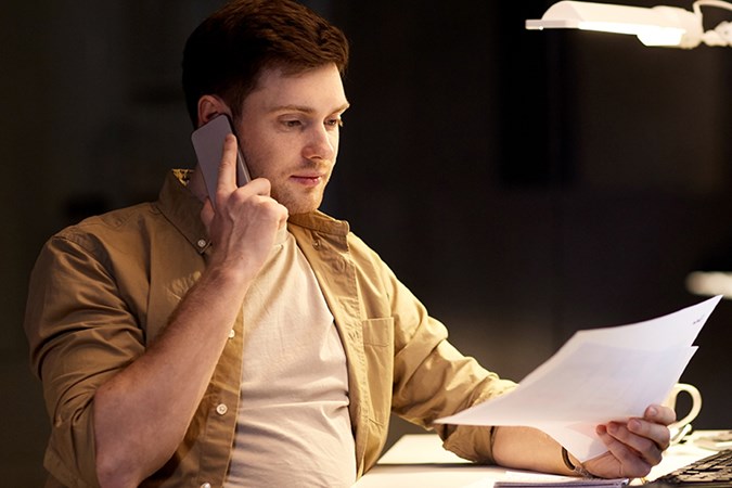 En man sitter vid ett skrivbord, talar i telefonoch håller i en faktura.