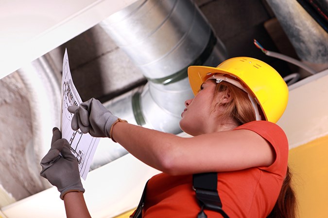 Kvinnlig ventilationstekniker som kontrollerar en installation av radonfläkt.